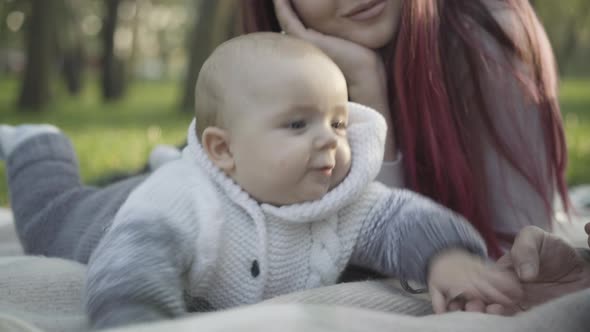 Closeup of Charming Cute Caucasian Boy Lying on Blanket Playing with Smiling Young Father and Mother alt