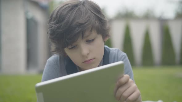 Close-up Portrait of Lonely Boy Using Tablet Outdoors. Unhappy Caucasian Schoolboy Spending Weekends alt