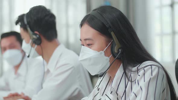 A Woman Of Three Asian Call Centre Agents In Mask Speaking To Customer While Her Colleagues Talking alt