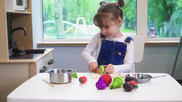 Happy Little girl playing with wooden natural toy food (vegetables) in a children's kitchen. Cute ho