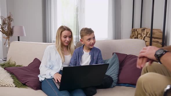 Wife and Her Cheery Son Sitting Together and Using Laptop and Greeting with High Five alt