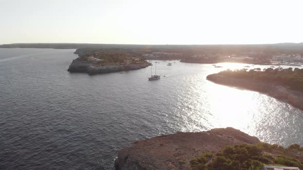 AERIAL: Mallorca coast at sunset and Sail Yacht float out of harbor bay alt