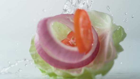 Fresh sliced vegetables falling on water surface. Slow Motion. alt