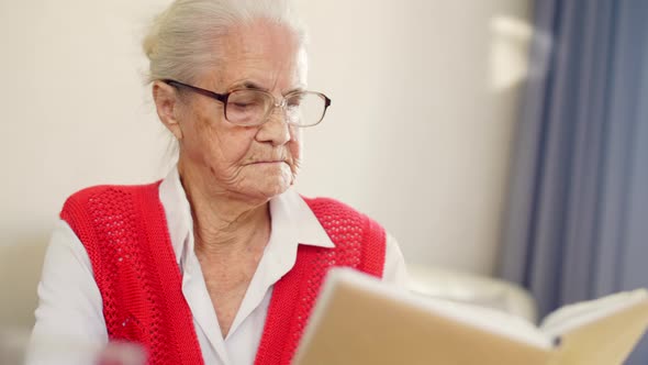 Elderly Woman in Glasses Reading a Book at Home