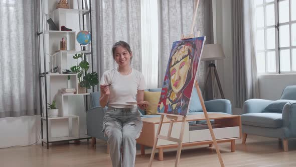 Asian Artist Girl Sitting And Holding Paintbrush, Wipe The Sweat And Smiling After Finish Painting alt