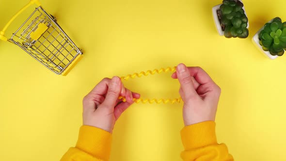 Hands of a young woman stretching a hair band on a bright yellow background with a mini grocery cart