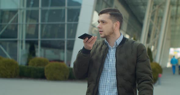 Man Using a Smartphone Voice Recording Function Online Walking on a City Street, Talking To Mobile alt
