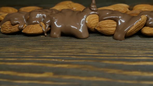 Milk Chocolate is Poured on Almonds on the Background of a Dark Wooden Table