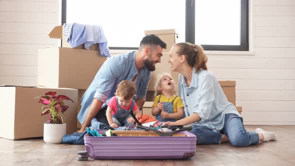 Caucasian Family, Man, Woman and Two Girls, Sit on Floor, Unpack Suitcase in New House. alt