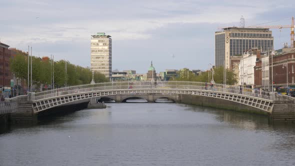 People Cross At Ha'penny Bridge Over Liffey River In Dublin, Ireland. - wide shot alt