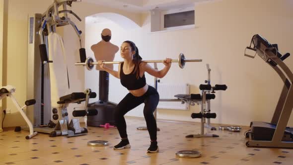 Wide Shot Portrait of Confident Focused Young Woman Doing Squats with Barbell in Gym alt