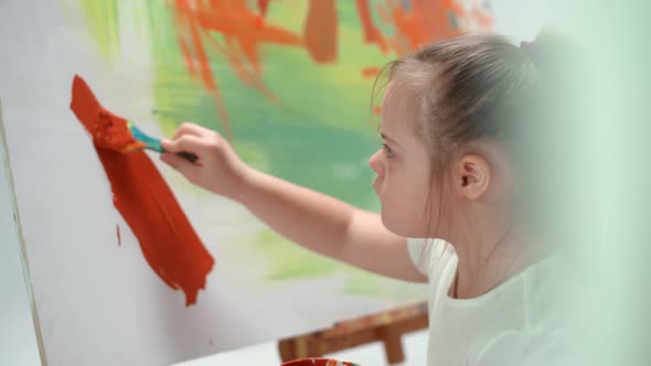 Girl with Down Syndrome Draws with a Brush on a Large Canvas in a White Room Kid Girl with Special alt