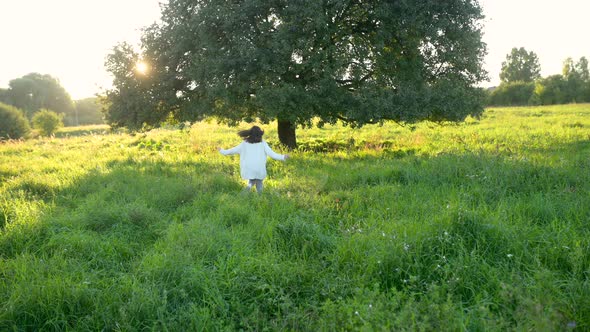 Happy little girl is playing and running in the field next to a lonely tree