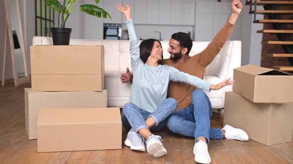 Happy Indian Newlyweds Moved in New Apartment Sitting on the Floor Among Cardboard Boxes in