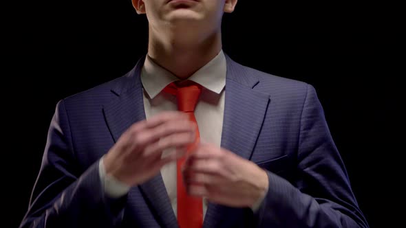 A Young Man in a Simple Blue Suit and White Shirt Neatly Straightens His Red Tie Hands alt