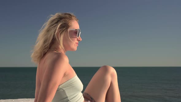Beautiful Blonde Woman in Sunglasses is Resting on the Background of the Sea alt