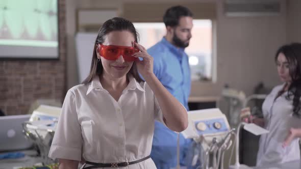Young Beautiful Female Dentist Putting on Protective Eyeglasses and Turning on Curing Lights As Her alt