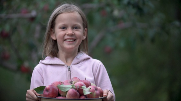 Happy child girl holding in hands a bowl of fresh red apples and smiling. Slow motion