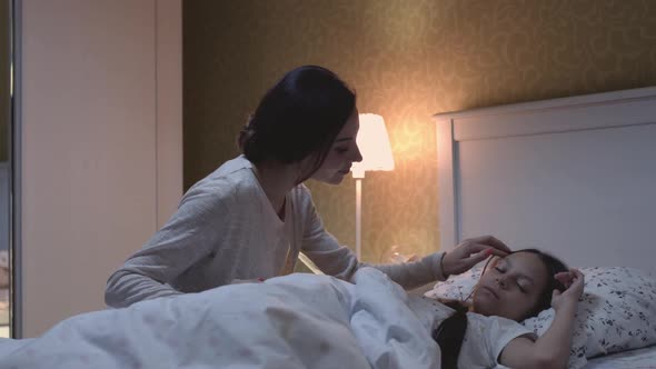 Mom with Caring Casual Life Sitting in Apartment Crib Children and Kissing alt