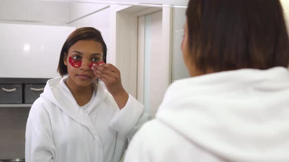 A Young Beautiful Woman Looks in the Mirror and Uses Eye Patches