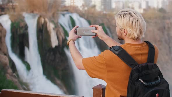 A Young Blonde Man Shoots a Waterfall on His Phone alt