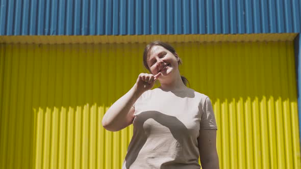 Woman Draws Heart Shape in Air Makes Heart From Hands Near Yellowblue Wall alt