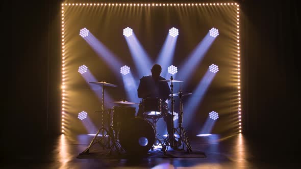 Silhouette Drummer Playing on Drum Kit on Stage in a Dark Studio with Smoke and Neon Lighting alt
