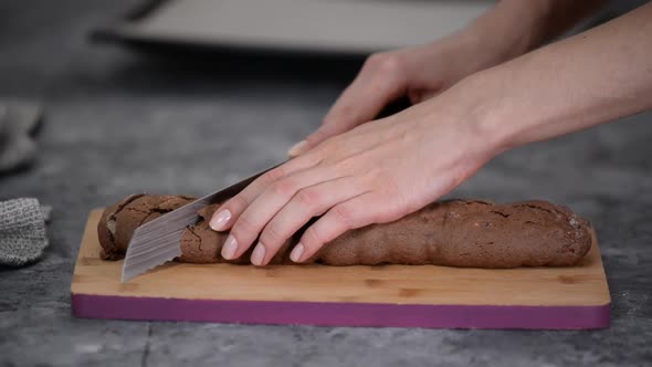 Chocolate hazelnut biscotti cookie , cutting with a serrated knife, on a wooden board.