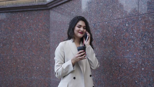 Joyful Young Girl Talks on the Phone with a Smile and Drinks Outdoor alt