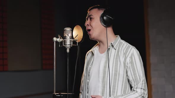Professional Male Singer is Performing a New Song With a Microphone While Recording in Music Studio