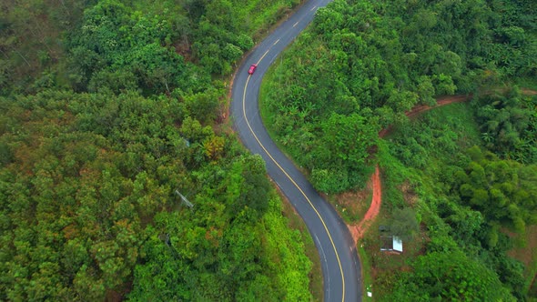 Aerial view over a winding road in the mountains of a tropical forest, Thailand. alt