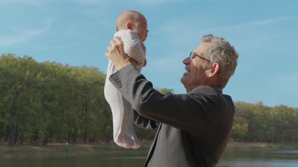 Senior Eldery Man Talking To His Baby Grandson, Holding Him in the Air, Close Up, Side View. alt