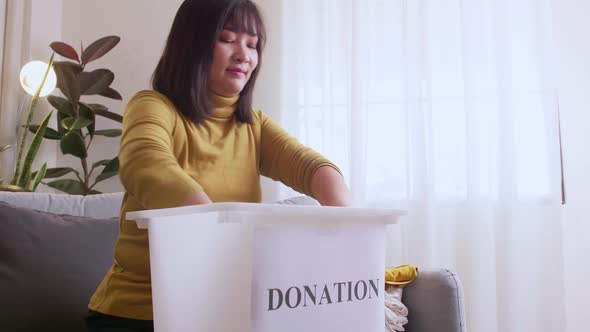 Woman selecting clothes for donation and putting in box. Concept campaign to donate unused items. alt