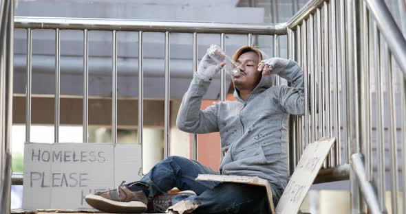Homeless man sitting and drink water on the overpass alt