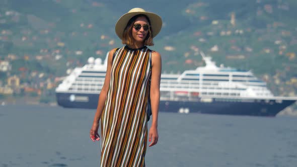 A woman on rocks with a cruise ship traveling in a luxury resort town in Italy, Europe alt