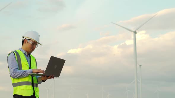 young male engineer working with laptop computer against wind turbine farm