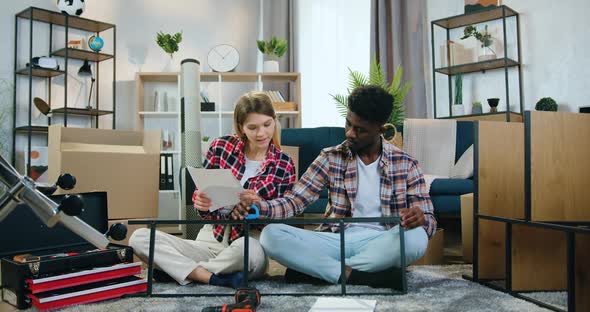 Mixed Race Pair Sitting on the Floor and Measuring Iron Construction with Tape Measure alt