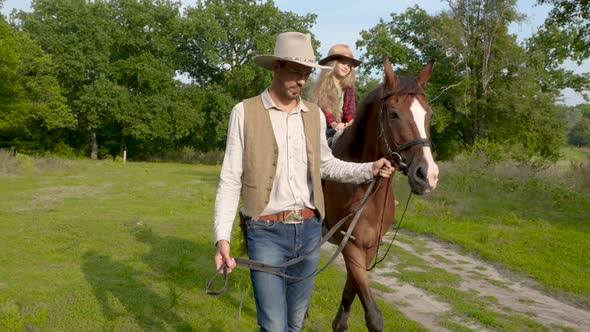A Young Cowboy is Leading a Horse on Which His Daughter is Sitting alt