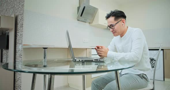Happy asian guy with headphones talks to friends online at home alt