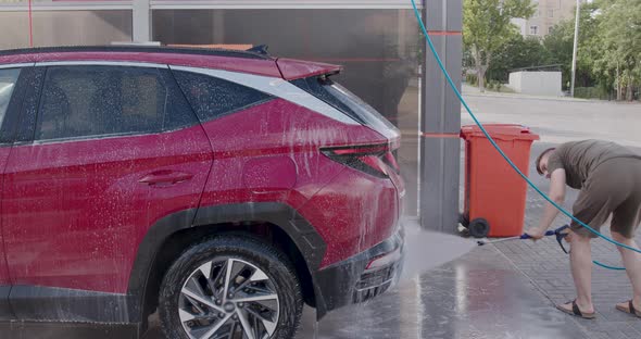 Young Boy Washes His Car with Pressurized Water at a Selfservice Car Wash alt