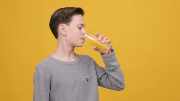 Teen Boy Drinking Orange Juice Smiling To Camera Yellow Background alt