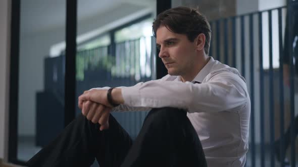Sad Caucasian Handsome Employee Sitting on Office Floor Sighing Thinking alt