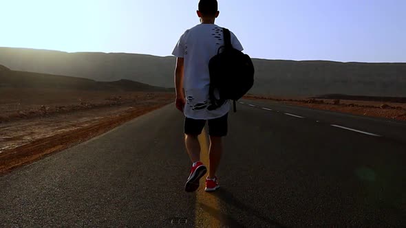 Man Walks Along an Asphalt Road with a Backpack on His Back Overlooking the Mountains