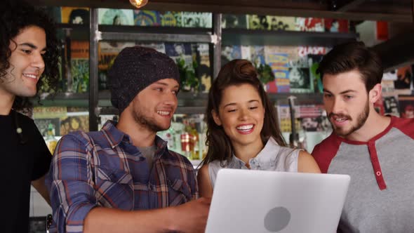 Friends interacting with each other while using laptop in pub alt