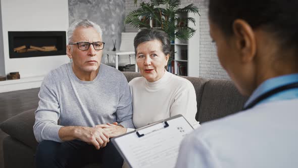 Doctor Female Announcing Good Test Results to Happy Elderly Patient and His Wife Who Sitting on Sofa alt