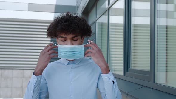 Young African American Man Putting on Medical Mask Looking to Camera at City Street alt