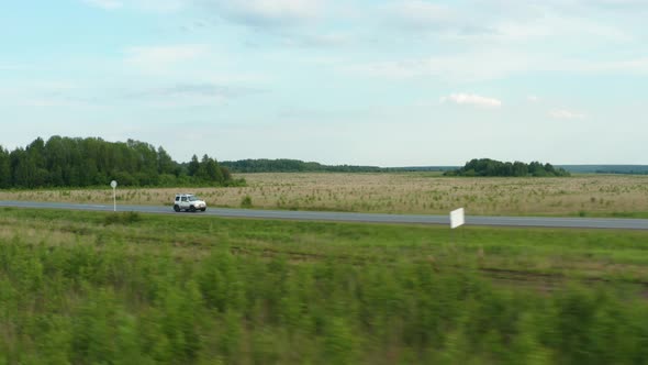 Aerial View of a Car Driving Along the Road Among Fields of Green Grass