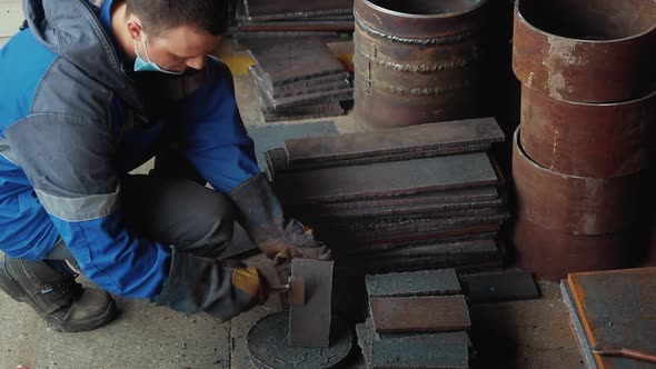 Worker in Heavy Industry or Metallurgy Beats Scale Off Iron Plates with Hammer