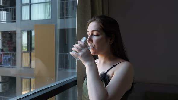 Happy Lady Drinks Water Looking Outside Window in Hotel Room alt