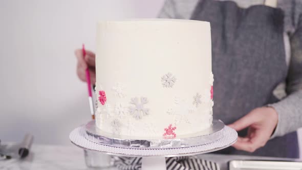Step by step. Decorating round funfetti cake with pink and white fondant snowflakes. alt